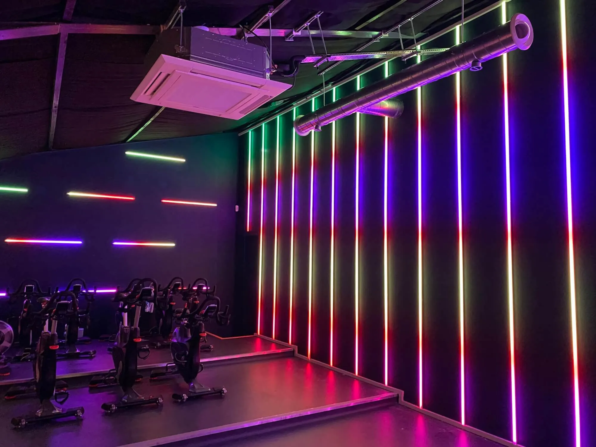 A row of exercise bikes in a gym with neon lights.