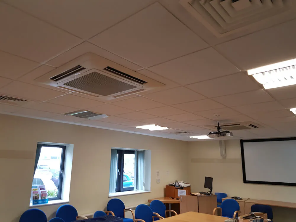 A classroom with a projector screen and blue chairs.